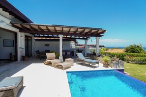 Ein überdachter Außenbereich mit Pool, Liegestühlen und einer Pergola.