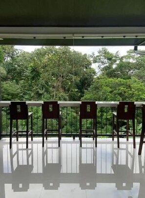Un balcon avec quatre chaises en bois et une table blanche, donnant sur une forêt verdoyante et luxuriante.