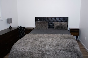 Un dormitorio con cabecera capitonada, alfombra mullida y cómoda de madera oscura.