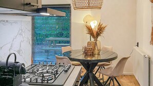 Una cocina moderna con estufa a gas, una mesa redonda con sillas, un jarrón decorativo con plantas secas y una lámpara colgante original.