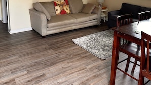 A living room with a beige sofa, a dining table with chairs, a ceiling fan, and three framed pictures on the wall. - Trail 10 Hideaway, Entire Apartment in Freeman, WV (Bramwell)