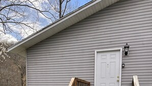 A wooden staircase leading to a white door on a gray building with a river in the background. - Trail 10 Hideaway, Entire Apartment in Freeman, WV (Bramwell)