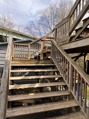 A wooden staircase with a metal railing, leading to a building with a green roof. - Trail 10 Hideaway, Entire Apartment in Freeman, WV (Bramwell)