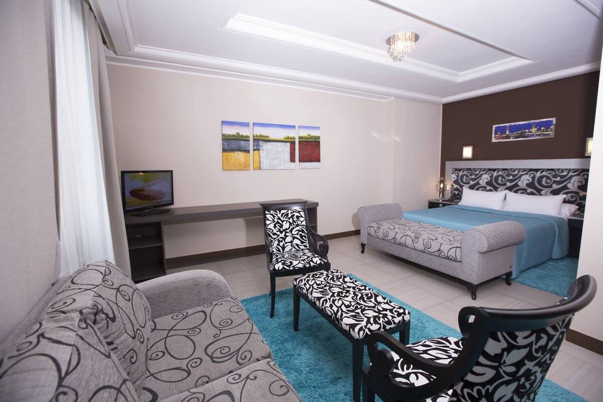 A hotel room with a bed, a sofa, a chair, a desk, and a television.