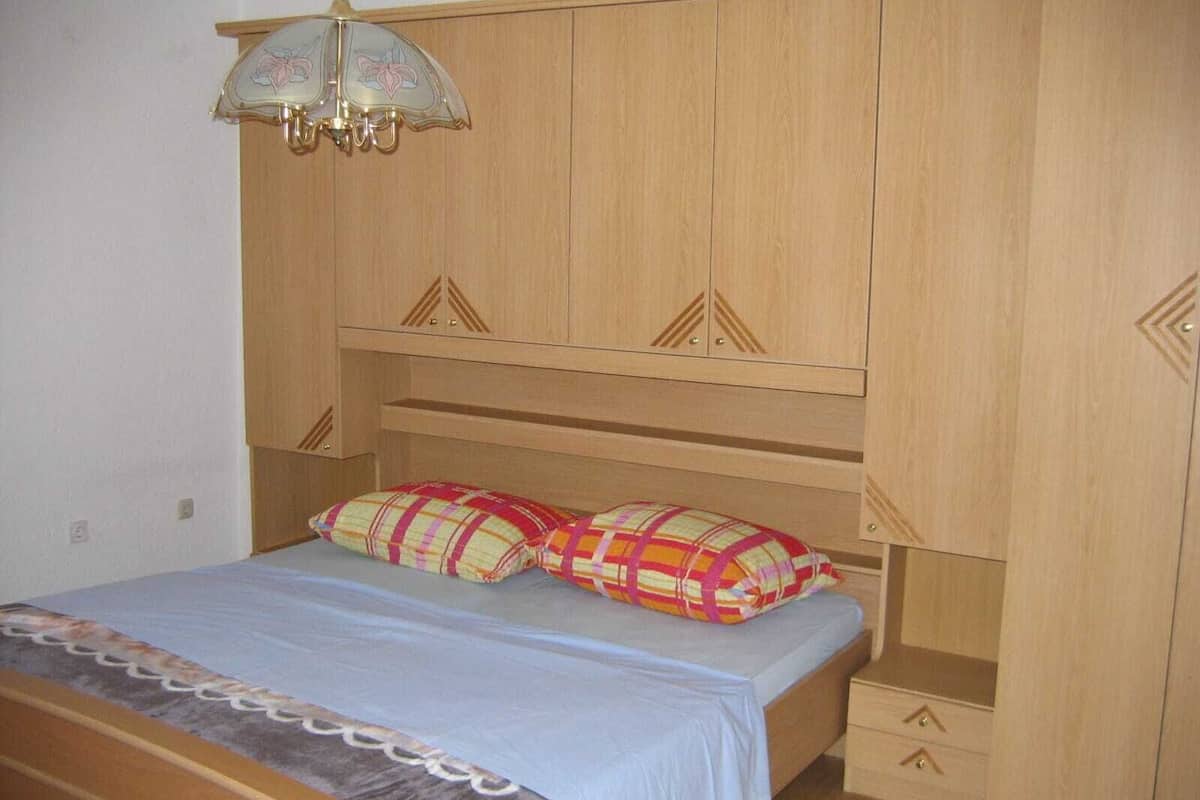 A bedroom with a bed, a nightstand, a wooden wardrobe, and a ceiling light fixture.
