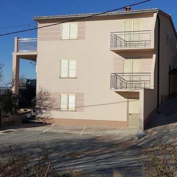 Un edificio de dos plantas con techo plano, varias ventanas con contraventanas y balcones con barandillas de metal.