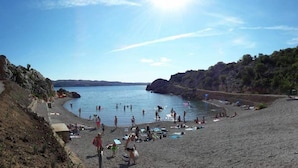 Una playa con gente nadando y tomando el sol, cielo despejado y acantilados rocosos.
