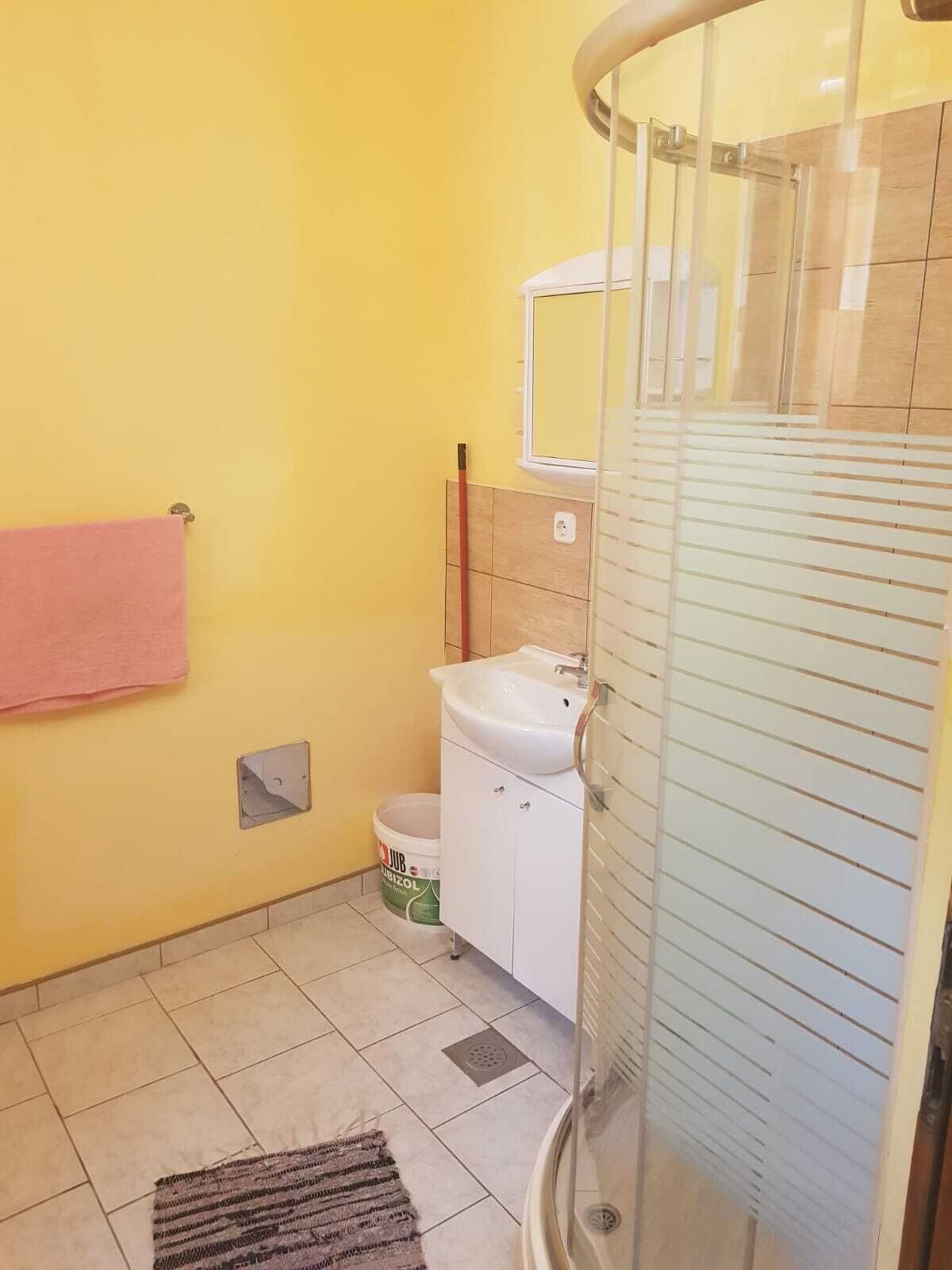 A bathroom with yellow walls, a white sink, a mirror, and a shower enclosure.
