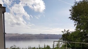 Vista de un lago con montañas al fondo, una escalera que lleva a un edificio y algo de vegetación en primer plano.