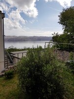 Vista de un lago con montañas al fondo, una escalera que lleva a un edificio y algo de vegetación en primer plano.