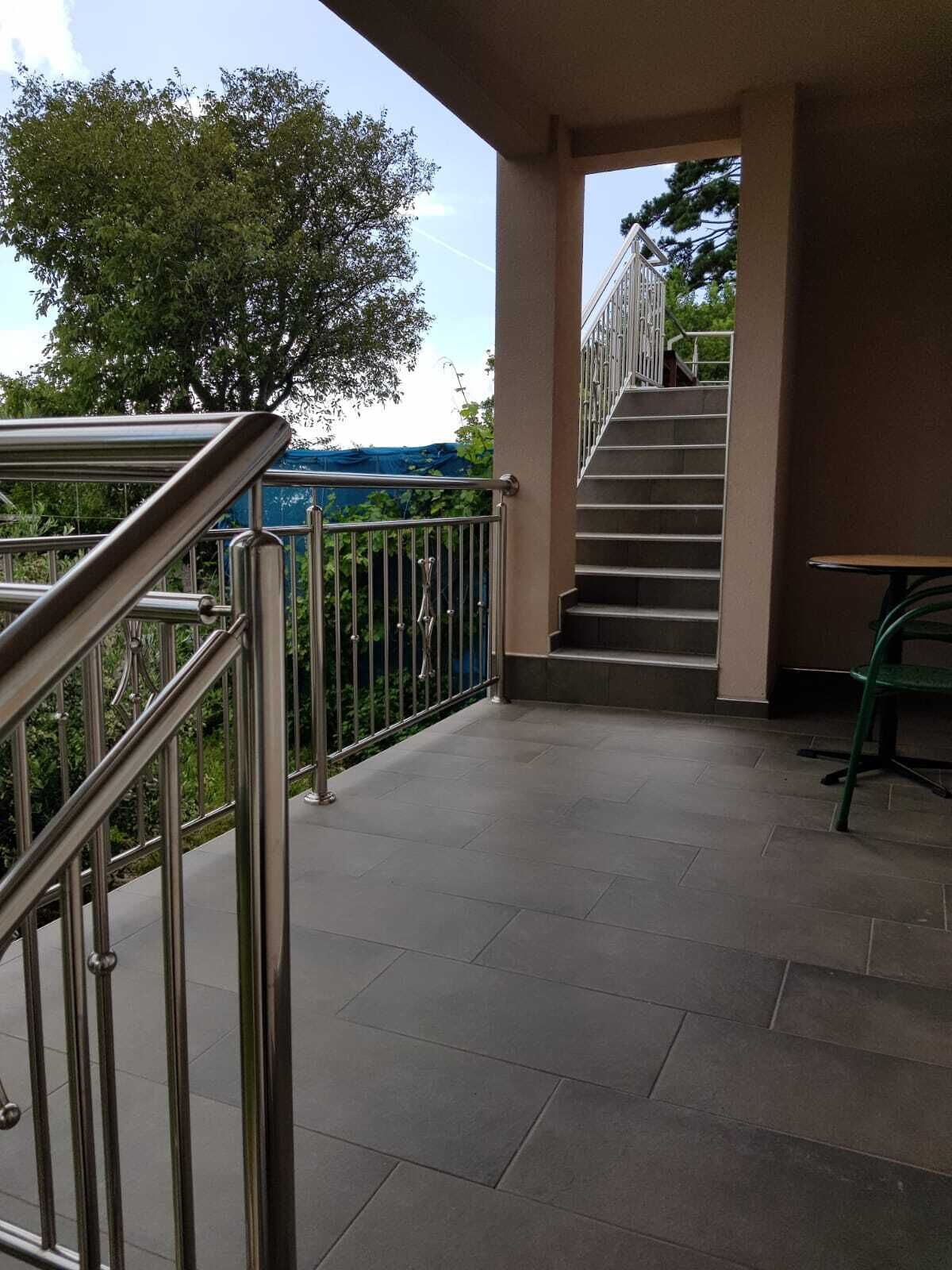 A covered outdoor area with a metal railing, a staircase leading to an upper level, and a green chair.