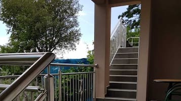 A covered outdoor area with a metal railing, a staircase leading to an upper level, and a green chair.
