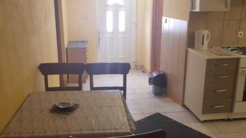 Une cuisine compacte avec un coin repas, dotée d’un sol carrelé, d’une petite table avec des chaises, d’une cuisinière et de placards.