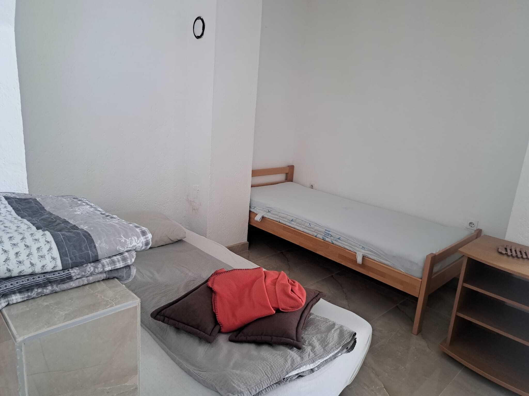 A small, simple room with a bed, a wooden bench, and a small table.