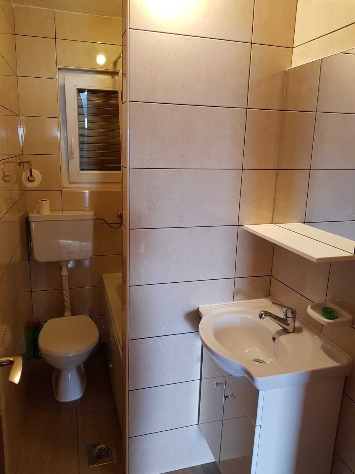 A bathroom with a toilet, sink, and a window above the toilet.