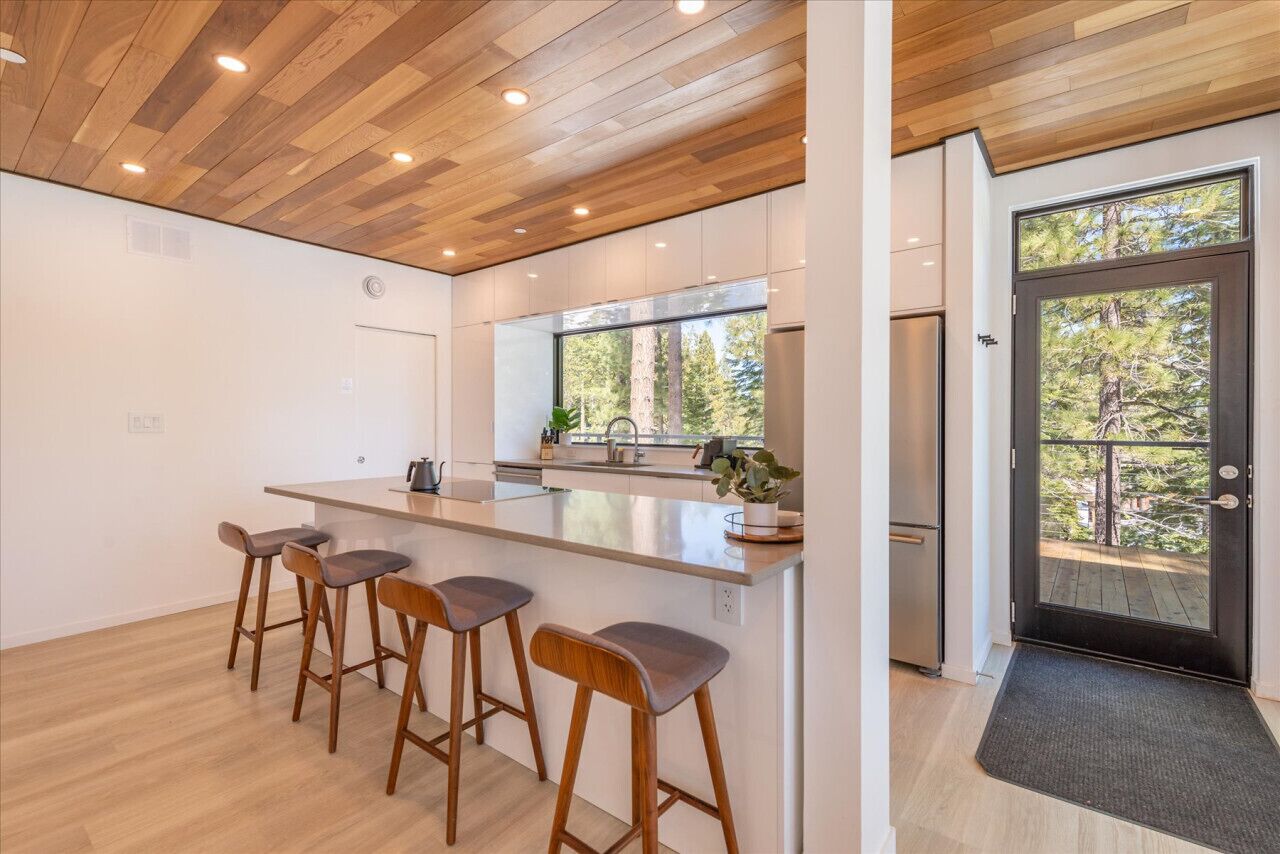 Une cuisine moderne avec un plafond en bois, une grande fenêtre et un coin bar avec des tabourets.