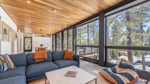 A modern living room with a wooden ceiling, large windows, a sofa, a coffee table, and a bean bag.