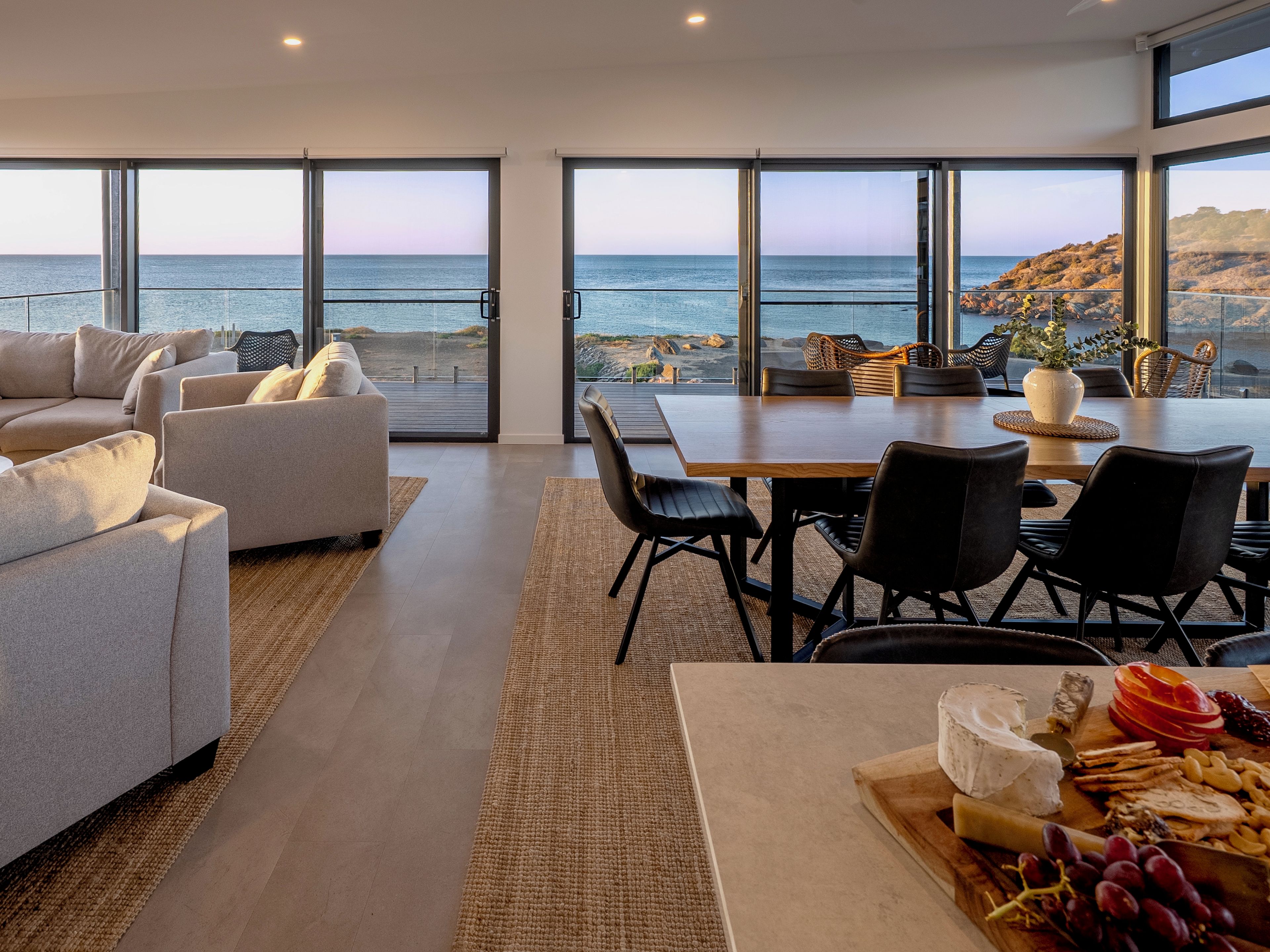 Ein modernes Wohnzimmer mit großem Esstisch, bequemen Sitzmöglichkeiten und einem weiten Blick auf das Meer durch große Fenster.
