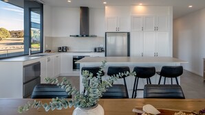 A modern kitchen with white cabinets, a central island with bar stools, and a view of the outdoors. - Cove Landing Ocean View Apt-01 Karatta Sleeps 4 (Penneshaw)