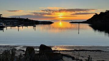 A sunset over a calm body of water with a pier and rocky shoreline.
