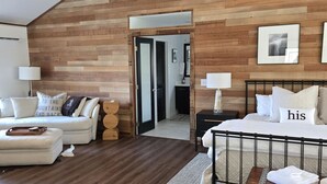 Une chambre moderne avec un plafond en pente, des murs recouverts de panneaux de bois, un lit avec un cadre en métal, une table de chevet, une commode et un canapé avec des coussins.