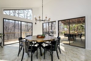 A spacious dining area with a round table and chairs, large windows, and a view of the outdoors.