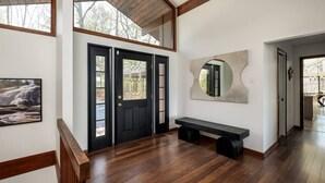 Un intérieur moderne avec un banc en bois, une porte noire dotée de panneaux de verre et un grand miroir mural.