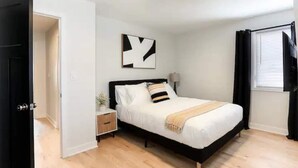 A bedroom with a bed, bedside table, and a wall-mounted artwork. - Lofty Urban Retreat (Bridgeview)