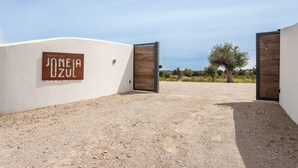 A building entrance with a sign reading "Quinta da Janeia Azul" and a gravel driveway leading to a wooden door. - Quinta da Janela Azul - Limão (Tavira)