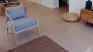 A modern living room with a wooden dining table, a blue cushioned chair, a woven rug, and a minimalist decor. - Quinta da Janela Azul - Limão (Tavira)