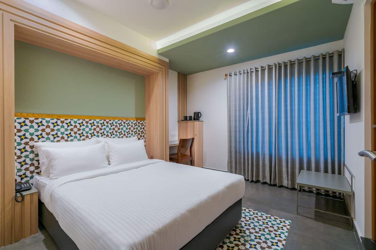 A hotel room with a large bed, a desk, a chair, a television, and a window with curtains.