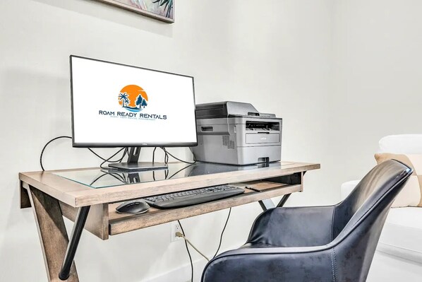 A modern office desk with a Dell monitor, Brother printer, and a black leather chair.