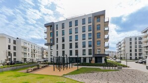 A modern multi-story residential building with balconies, a central courtyard with exercise equipment, and a parking area. - Golden Azzure by Grand Apartments (Gdansk)