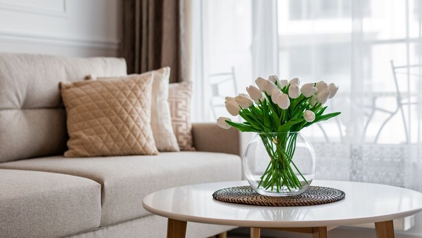 A living room with a beige sofa, a round coffee table, and a vase with white tulips. - Golden Azzure by Grand Apartments (Gdansk)