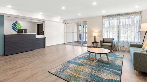 A spacious lobby with a reception desk, a seating area with a table and chairs, and a large window with curtains. - Woodspring Suites Savannah West Chatham Parkway (Savannah)