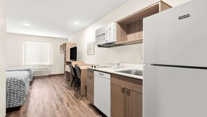 A compact kitchen with a microwave, sink, and dishwasher, wooden cabinets, and a built-in TV. - Woodspring Suites Savannah West Chatham Parkway (Savannah)