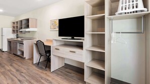 A modern kitchen with a built-in stove, oven, and sink, a dining area with a chair, and a TV on a wooden shelf. - Woodspring Suites Savannah West Chatham Parkway (Savannah)