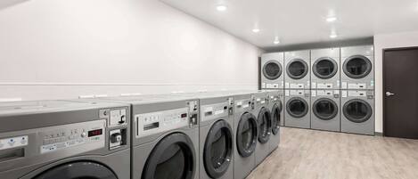 A row of front-loading washing machines in a well-lit laundry room with a wooden floor.