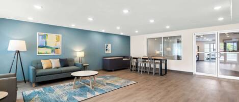 Un espacio de oficina moderno con una pared azul de acento, un sofá, una zona de comedor y un gran ventanal.