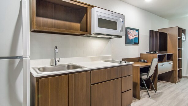 A compact kitchen with a built-in microwave, a sink, and wooden cabinets. - WoodSpring Suites Winston-Salem near Hanes Mall (Winston-Salem)