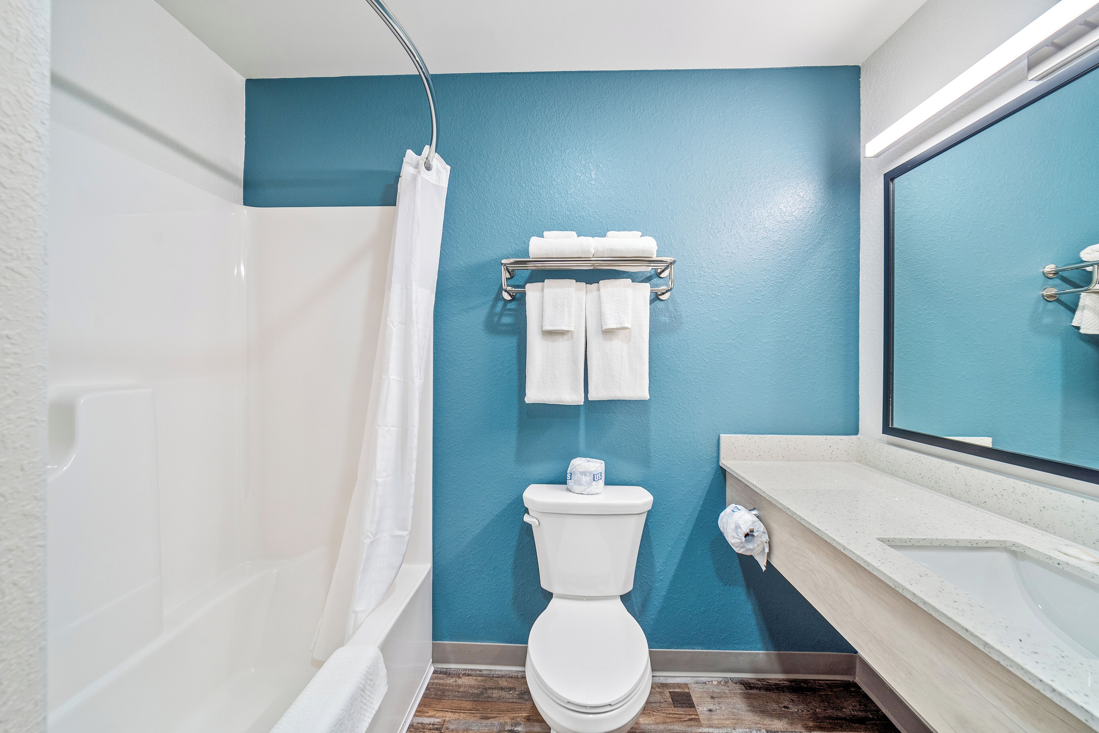 Een badkamer met een wit toilet, blauwe wanden, een witte badkuip en een witte wastafel met spiegel.