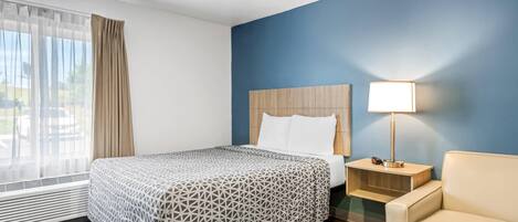 A hotel room with a bed, a nightstand with a lamp, a chair, and a window with curtains.