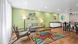 A modern living room with a sofa, chairs, a coffee table, and a dining area with a table and chairs. - WoodSpring Suites Winston-Salem near Hanes Mall (Winston-Salem)