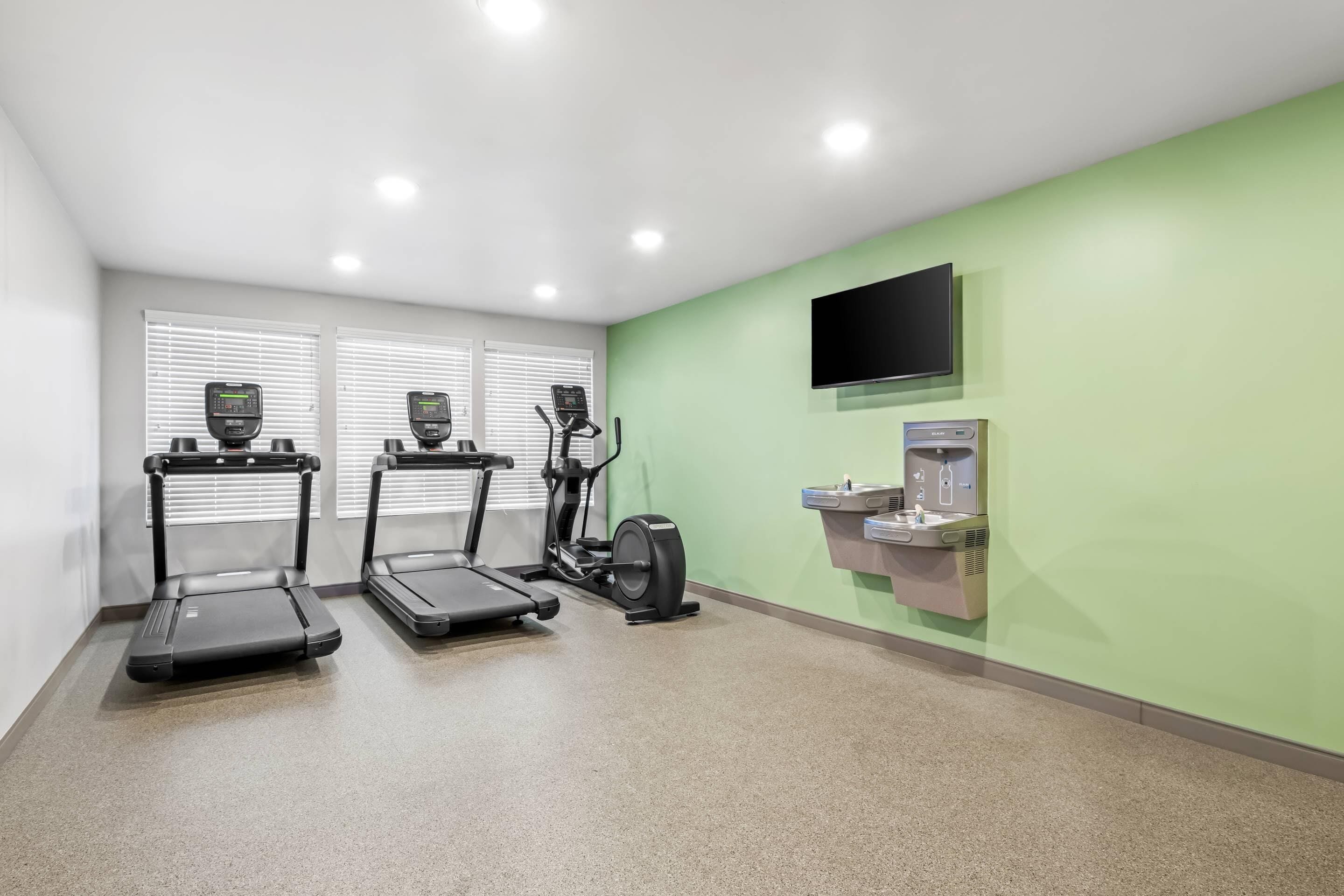 A fitness room with treadmills, a stationary bike, and a water dispenser.