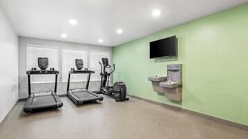 Un gimnasio con cintas de correr, una bicicleta estática y un dispensador de agua.