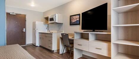 Una habitación funcional con kitchenette, una cama, un escritorio y un televisor.