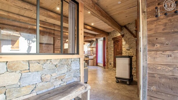 Interior em madeira com paredes de pedra, um banco e uma área de cozinha visível por uma janela.
