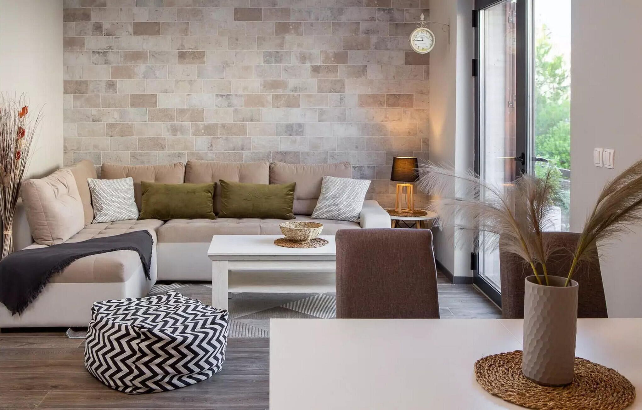 Ein modernes Wohnzimmer mit Steinwand, einer Couch, einem Couchtisch und Blick durch ein großes Fenster.