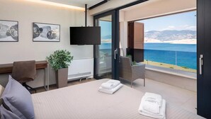Een moderne hotelkamer met een groot bed, een bureau, een flatscreen televisie en een balkon met uitzicht op zee.