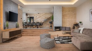 Een moderne woonkamer met een open haard, een bank, een salontafel en een aan de muur bevestigde televisie.